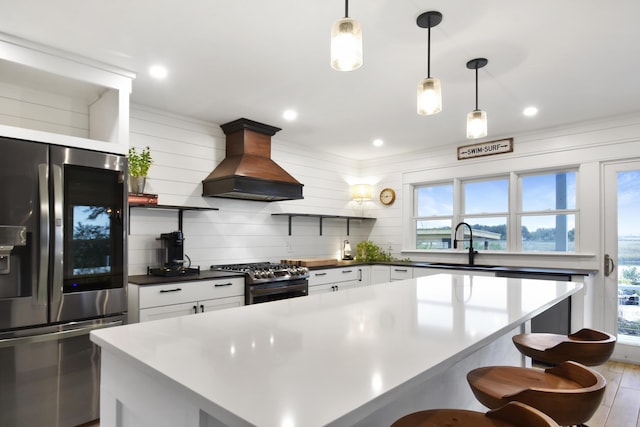 kitchen featuring appliances with stainless steel finishes, sink, white cabinets, custom exhaust hood, and hanging light fixtures