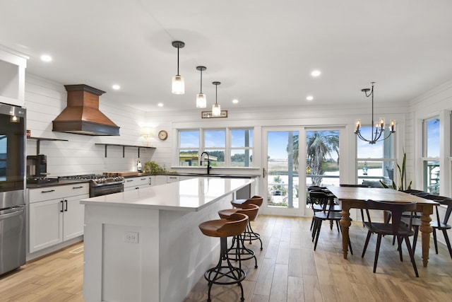 kitchen with hanging light fixtures, white cabinetry, stainless steel range with gas cooktop, and custom range hood