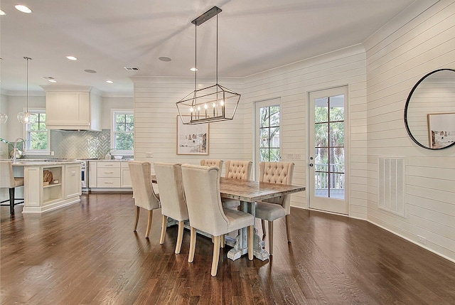 dining space with crown molding, dark wood-type flooring, wood walls, and an inviting chandelier