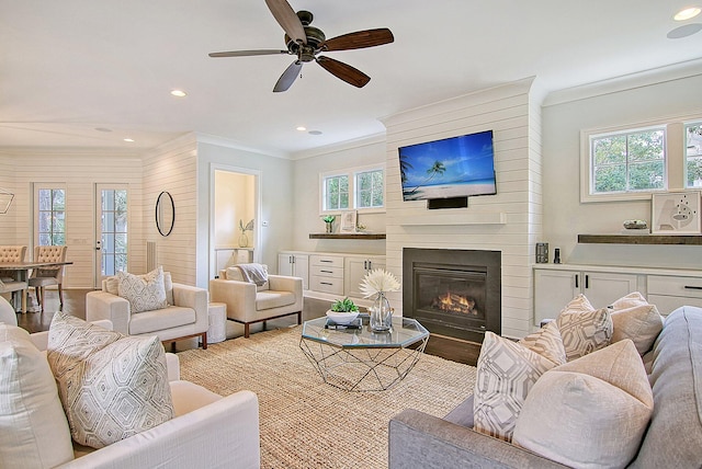 living room featuring wood-type flooring, a fireplace, ornamental molding, and ceiling fan