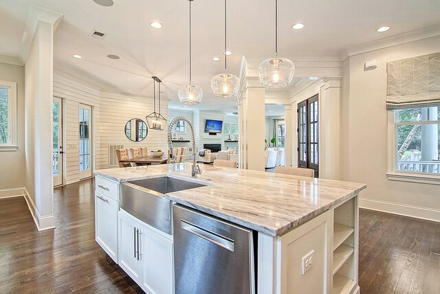 kitchen with hanging light fixtures, light stone counters, an island with sink, and stainless steel dishwasher