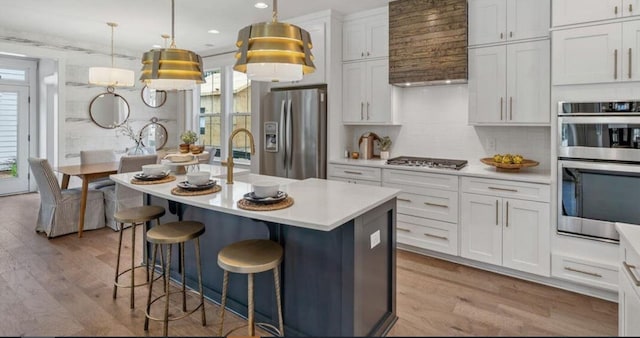 kitchen with appliances with stainless steel finishes, light countertops, white cabinets, a center island with sink, and light wood-style floors