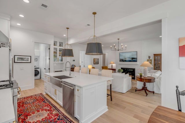 kitchen featuring washer / clothes dryer, an island with sink, white cabinetry, a fireplace, and sink