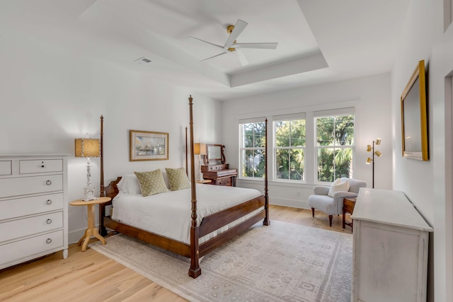 bedroom with light hardwood / wood-style flooring, a tray ceiling, and ceiling fan