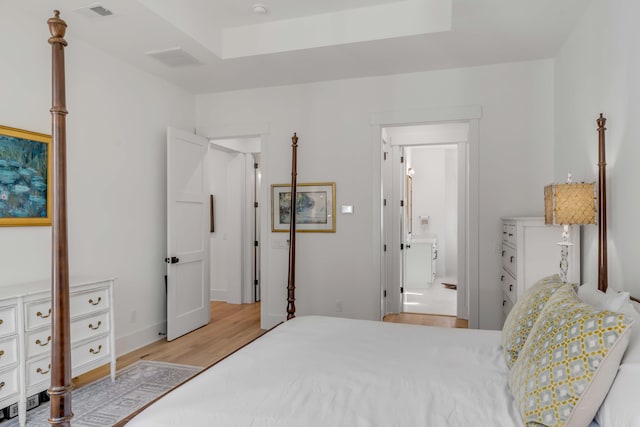 bedroom with connected bathroom, a raised ceiling, and light wood-type flooring