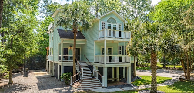 view of front of property featuring gravel driveway, stairway, a balcony, and covered porch