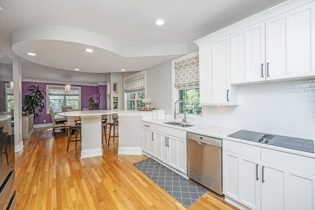 kitchen featuring dishwasher, a sink, black electric cooktop, a breakfast bar, and light wood finished floors