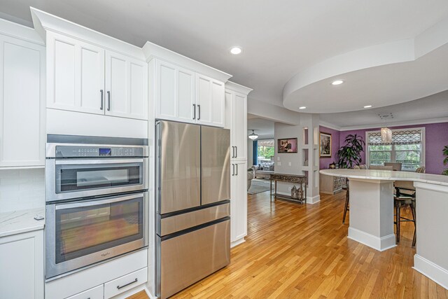 kitchen featuring stainless steel appliances, recessed lighting, light wood-style floors, a breakfast bar, and white cabinetry