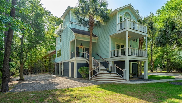 rear view of house featuring a balcony, gravel driveway, stairway, and a yard