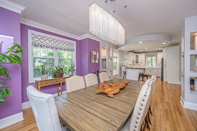 dining room with light wood-type flooring, a chandelier, baseboards, crown molding, and arched walkways