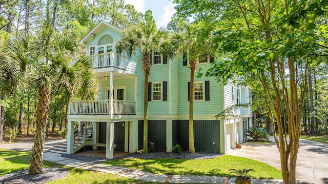 back of property featuring a balcony, stairway, a garage, concrete driveway, and covered porch