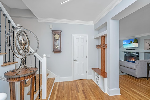 entryway with light wood-type flooring, stairway, crown molding, a glass covered fireplace, and baseboards
