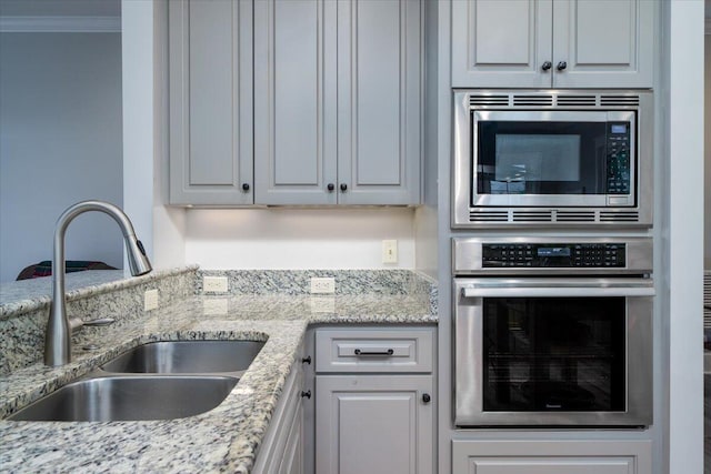 kitchen with crown molding, white cabinets, light stone counters, a sink, and appliances with stainless steel finishes