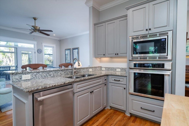 kitchen featuring crown molding, appliances with stainless steel finishes, a sink, a peninsula, and light wood-style flooring