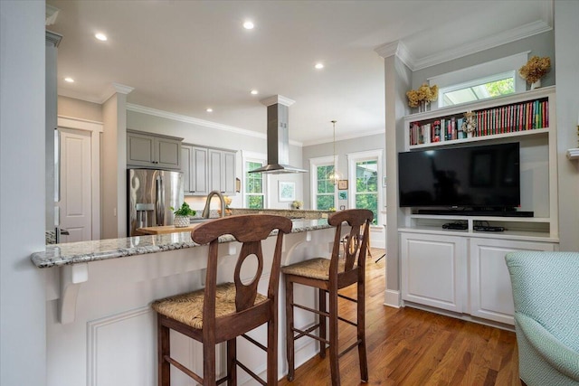 kitchen with light stone countertops, a breakfast bar area, dark wood finished floors, island exhaust hood, and stainless steel refrigerator with ice dispenser