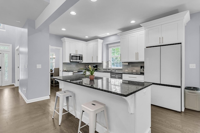 kitchen featuring a kitchen bar, appliances with stainless steel finishes, wood finished floors, a sink, and white cabinetry