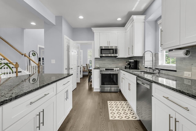 kitchen featuring appliances with stainless steel finishes, a sink, dark stone countertops, white cabinetry, and dark wood-type flooring