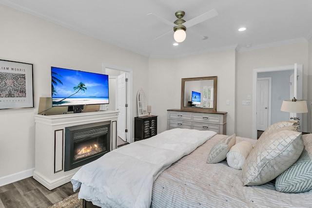 bedroom featuring a glass covered fireplace, recessed lighting, baseboards, wood finished floors, and ornamental molding