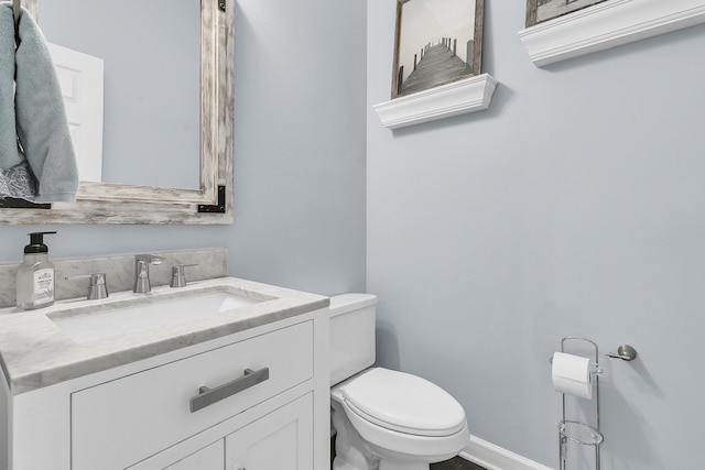 half bathroom with vanity, baseboards, and toilet
