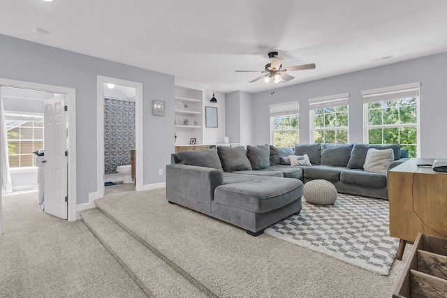 living area featuring carpet floors, built in shelves, a ceiling fan, baseboards, and visible vents