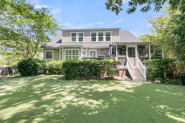 view of front of property with roof with shingles, stairs, a sunroom, and a front lawn