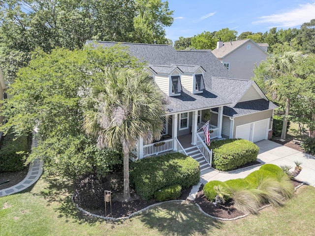 new england style home featuring a shingled roof, an attached garage, a porch, and driveway