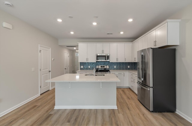 kitchen featuring a center island with sink, backsplash, stainless steel appliances, white cabinetry, and a sink