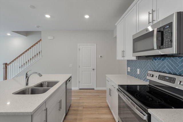 kitchen featuring stainless steel appliances, a sink, white cabinetry, light stone countertops, and tasteful backsplash