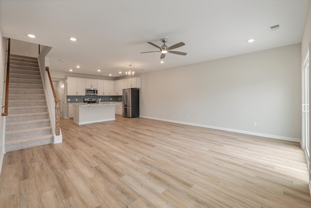 unfurnished living room featuring light wood finished floors, stairway, a ceiling fan, and baseboards