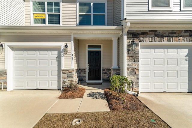 property entrance featuring a garage, stone siding, and driveway