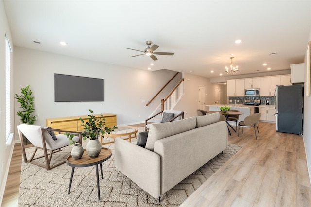 living area featuring recessed lighting, visible vents, stairs, light wood-type flooring, and ceiling fan with notable chandelier