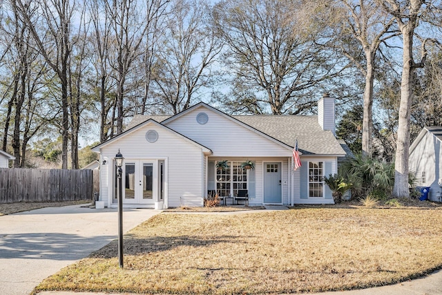 view of front of property featuring a shingled roof, fence, concrete driveway, french doors, and a chimney