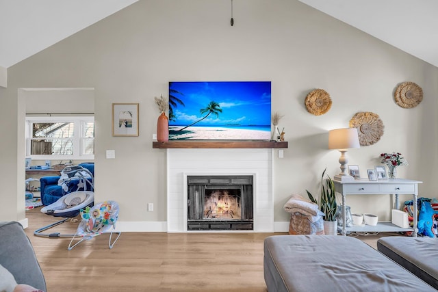 living room featuring a warm lit fireplace, high vaulted ceiling, wood finished floors, and baseboards