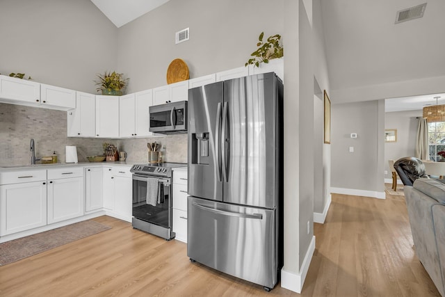 kitchen with high vaulted ceiling, stainless steel appliances, visible vents, white cabinetry, and light countertops