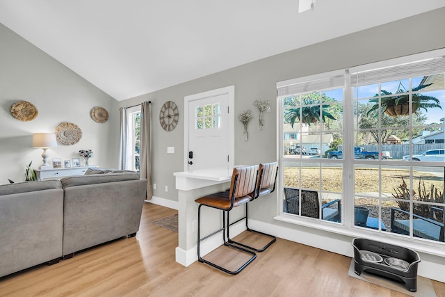 living area featuring light wood-style floors, baseboards, and vaulted ceiling