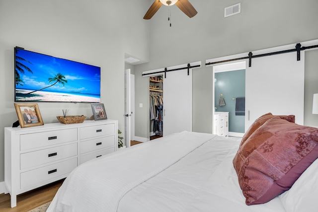 bedroom featuring a barn door, visible vents, a towering ceiling, ensuite bath, and wood finished floors