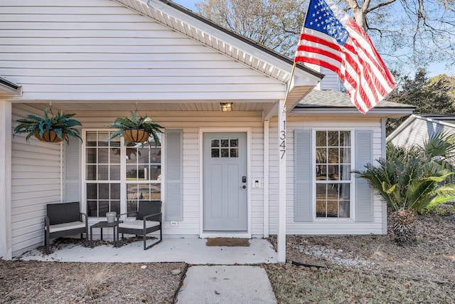 view of exterior entry with a porch and roof with shingles