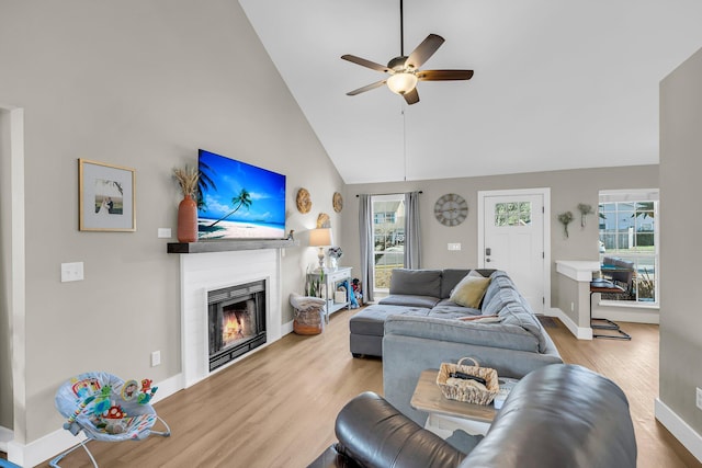 living area with ceiling fan, plenty of natural light, a lit fireplace, and wood finished floors