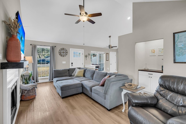 living area featuring ceiling fan, high vaulted ceiling, a fireplace, and light wood-style floors