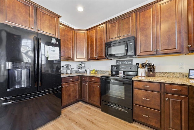 kitchen with light wood-type flooring, black appliances, light stone counters, and recessed lighting