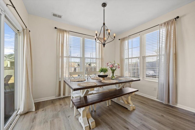 dining area featuring an inviting chandelier, baseboards, visible vents, and wood finished floors