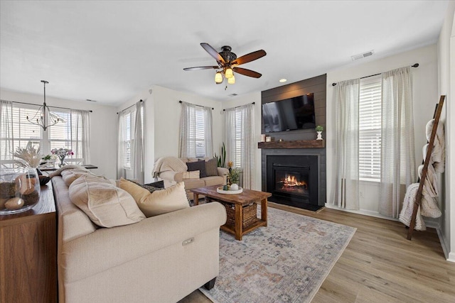 living area featuring light wood-style floors, a large fireplace, visible vents, and ceiling fan with notable chandelier