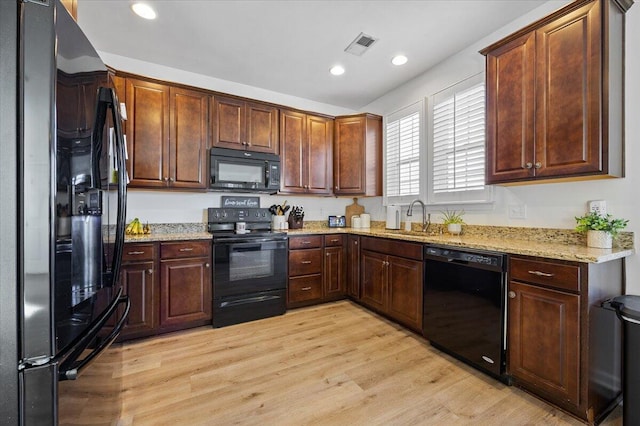 kitchen featuring visible vents, a sink, light wood finished floors, and black appliances