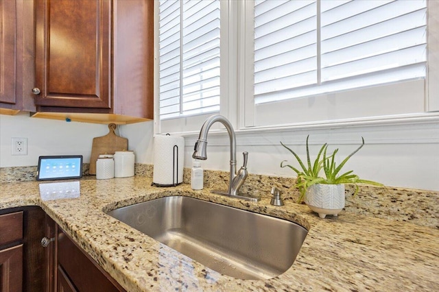 kitchen featuring a sink, dark brown cabinets, and light stone countertops