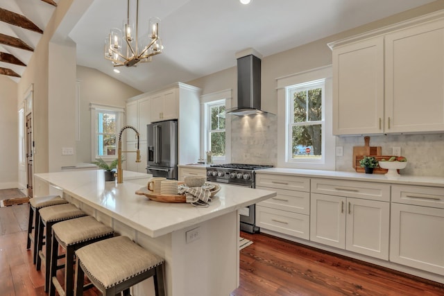 kitchen featuring stainless steel appliances, wall chimney range hood, plenty of natural light, and a kitchen island with sink