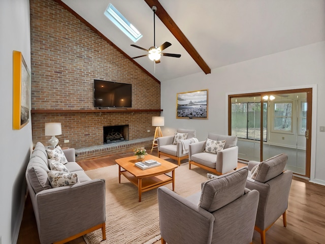 living room with a skylight, beamed ceiling, ceiling fan, a fireplace, and light hardwood / wood-style flooring