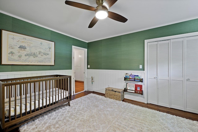 bedroom with crown molding, wood finished floors, a closet, a crib, and a wainscoted wall