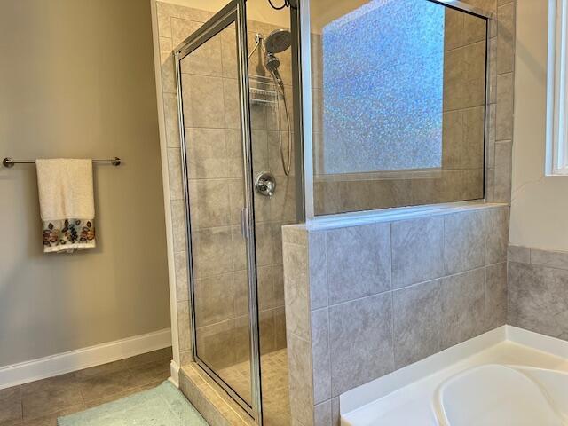 full bathroom featuring baseboards, tile patterned flooring, a garden tub, and a shower stall