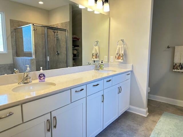 bathroom featuring baseboards, double vanity, a sink, and a shower stall