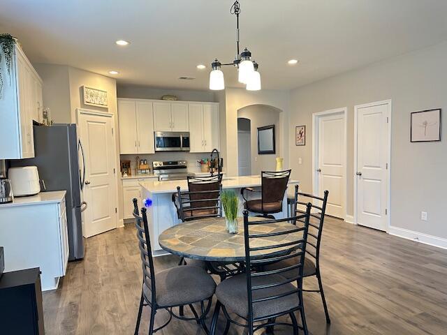 dining space featuring arched walkways, dark wood-style floors, and recessed lighting